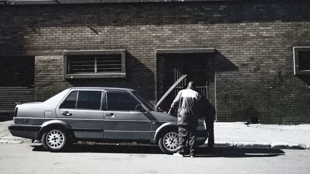 An old black and white image of two men attempting to repair a car. 