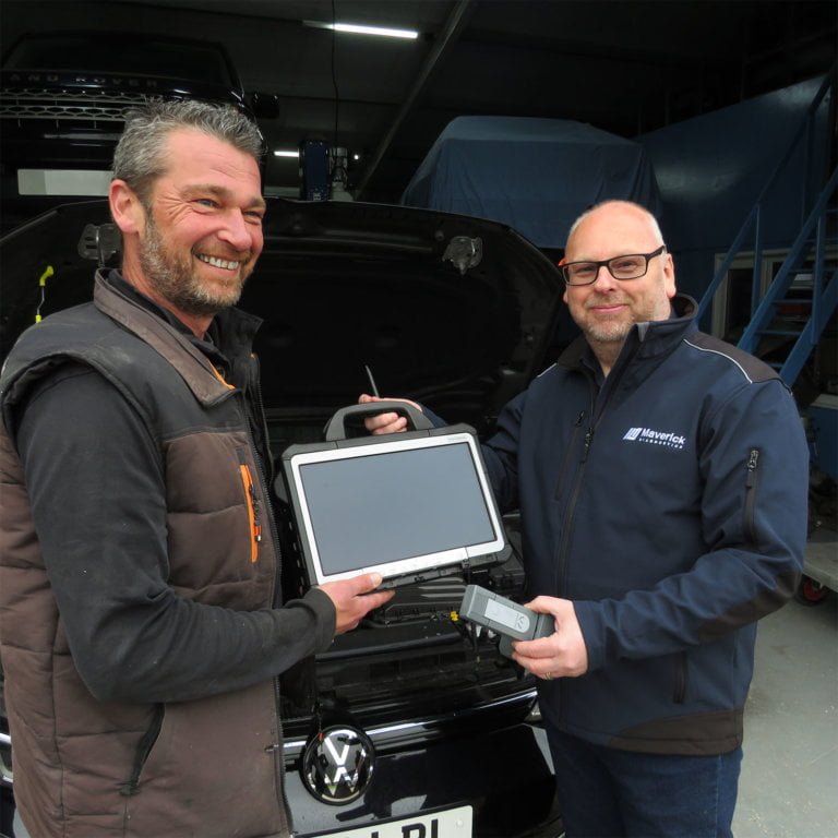Two men happily exchanging a tablet PC and diagnostic tool in front of a car